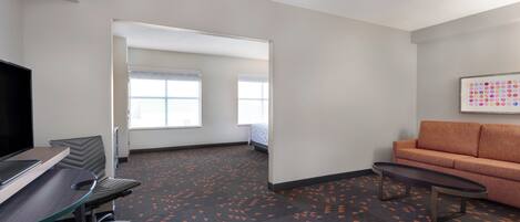 A hotel room with a desk, chair, sofa, and a painting on the wall.