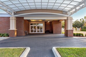 A covered entrance with a brick facade, glass doors, and a bench. - Holiday Inn Winter Haven by IHG (Winter Haven)