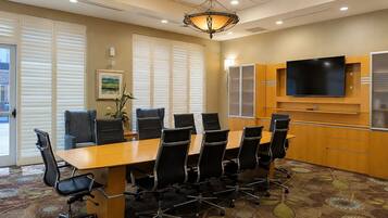 A conference room with a long table, black chairs, a flat-screen TV, and a chandelier.