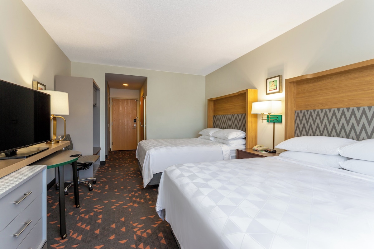 A hotel room with two beds, a desk with a computer, a TV, and a desk lamp.