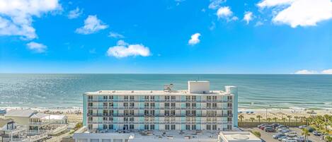 A multi-story hotel with a parking lot in front, overlooking a beach and the ocean.