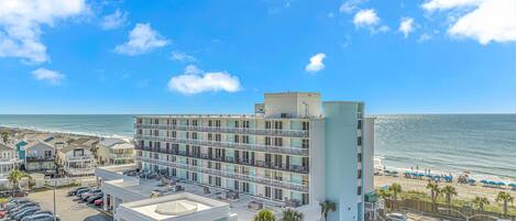 A multi-story hotel with a parking lot and beach view.