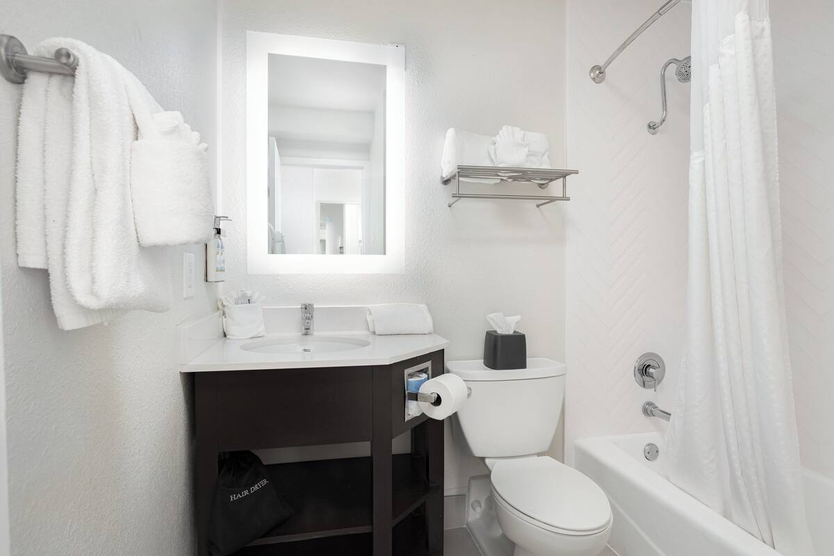 A modern bathroom with a white sink, toilet, and bathtub. There is a towel rack with towels, a mirror above the sink, and a shower curtain.