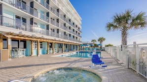 A hotel pool area with multiple pools, a hot tub, and a covered seating area.