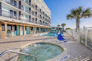 Zona de piscina de un hotel con varias piscinas, un jacuzzi y una zona de estar cubierta.