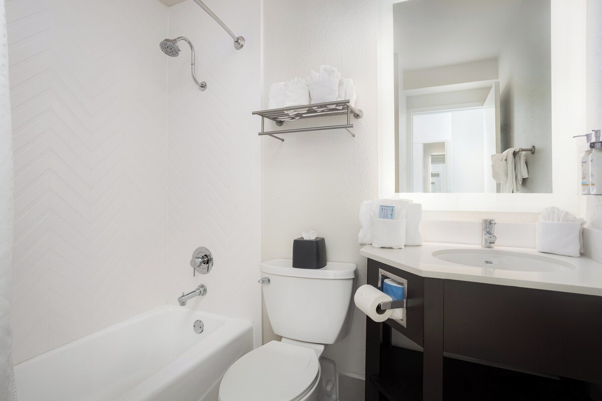 A modern bathroom with a white bathtub, a toilet, and a sink with a mirror above.