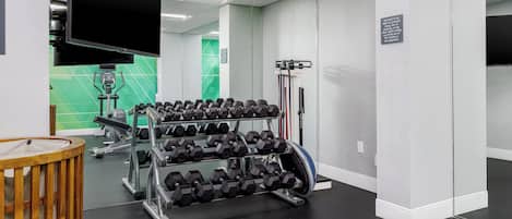 A gym with a mirrored wall, a television, and a rack of dumbbells.
