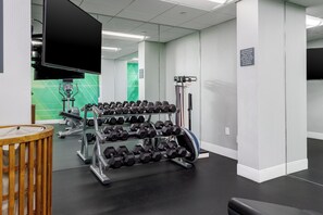 A gym with a mirrored wall, a television, and a rack of dumbbells.