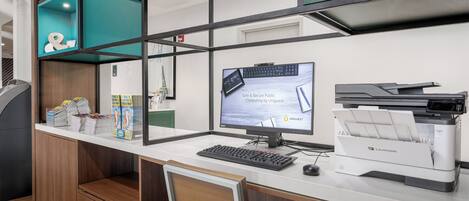 A modern office workspace with a desk, computer, printer, and a teal-colored storage unit.