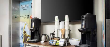 A coffee station with two coffee makers, a kettle, and a stack of disposable cups.