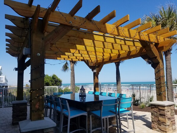 An outdoor seating area with a wooden pergola, stone pillars, and blue chairs.