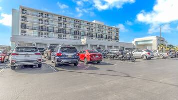A parking lot with multiple cars and a motorcycle, a multi-story building with balconies, and a clear blue sky.