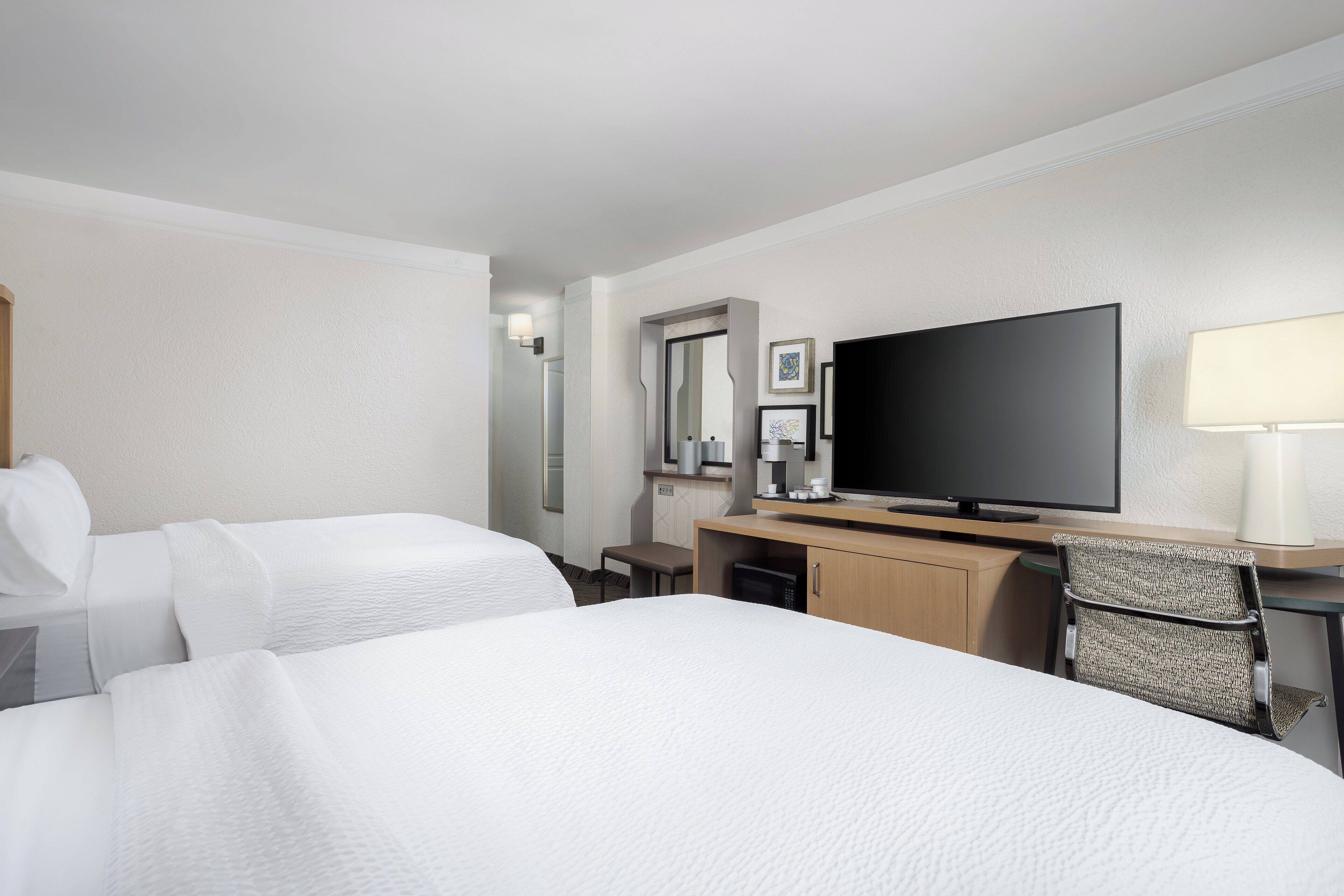 Een hotelkamer met twee bedden, een bureau met een televisie, een stoel en een kleine tafel met een lamp.