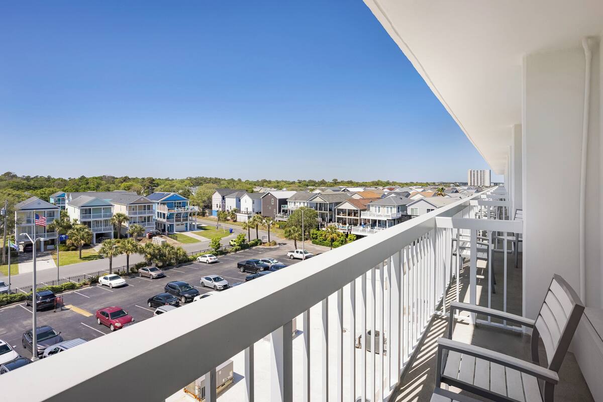 A balcony with a view of a parking lot and buildings.