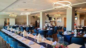 Un comedor amplio con largas mesas dispuestas para varios invitados, con sillas azules, manteles blancos y centros de mesa florales.
