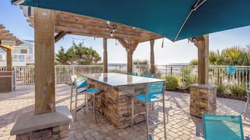 An outdoor patio area with a stone bar, two blue chairs, and a large umbrella.
