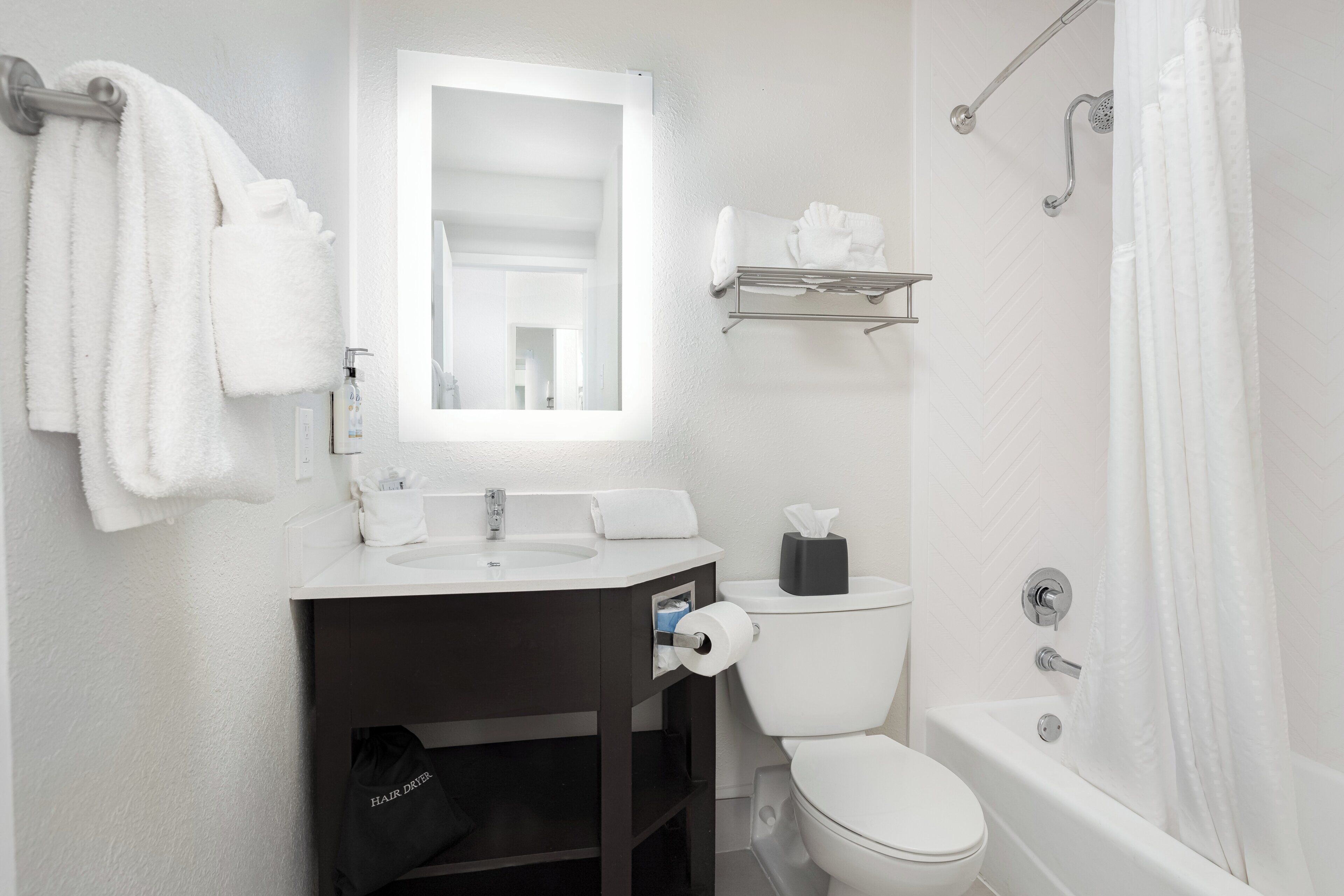 A modern bathroom with a white sink, toilet, and bathtub. There is a towel rack with towels, a mirror above the sink, and a shower curtain.