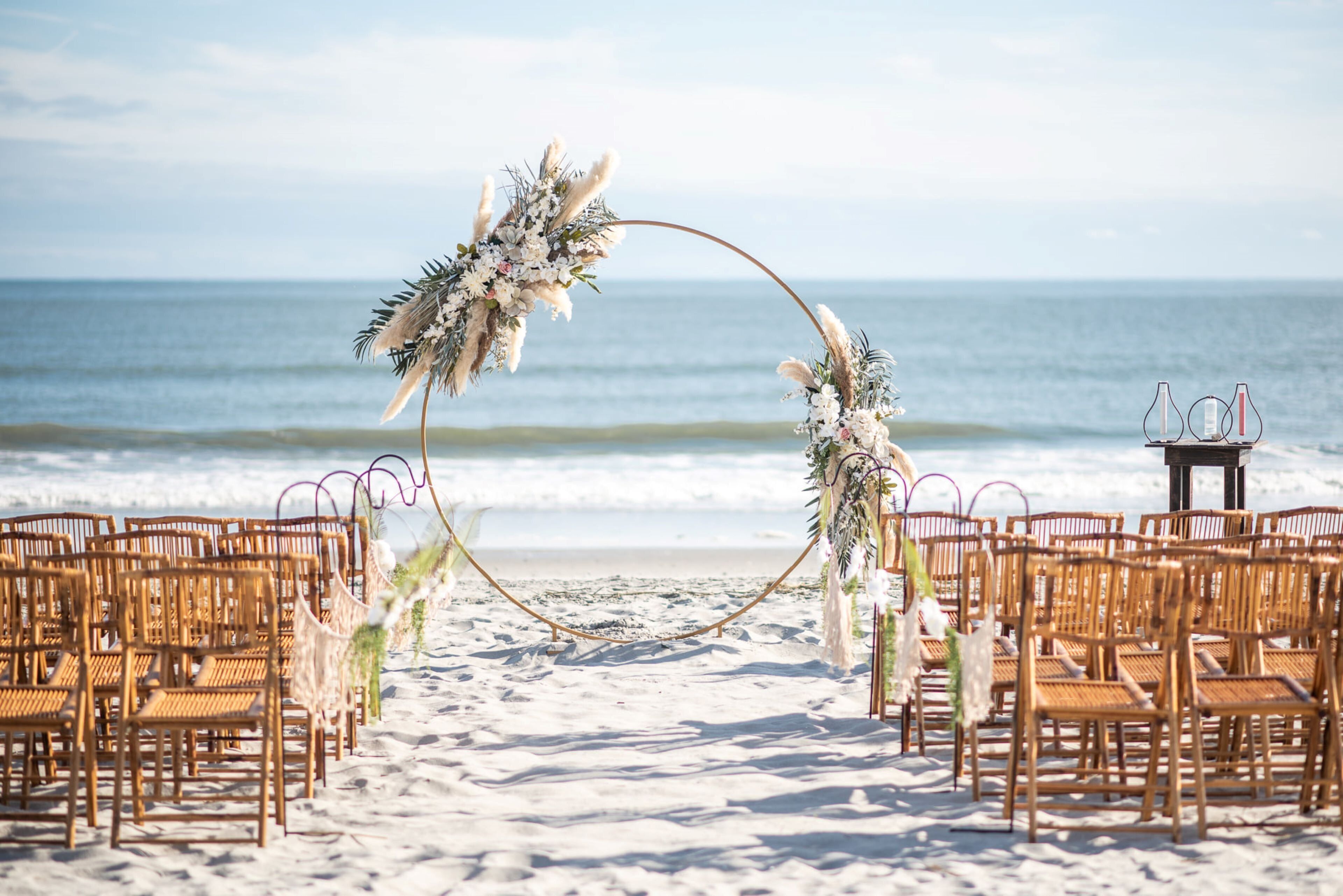 Une cérémonie de mariage organisée sur la plage, avec une arche décorée de fleurs et des chaises en osier.
