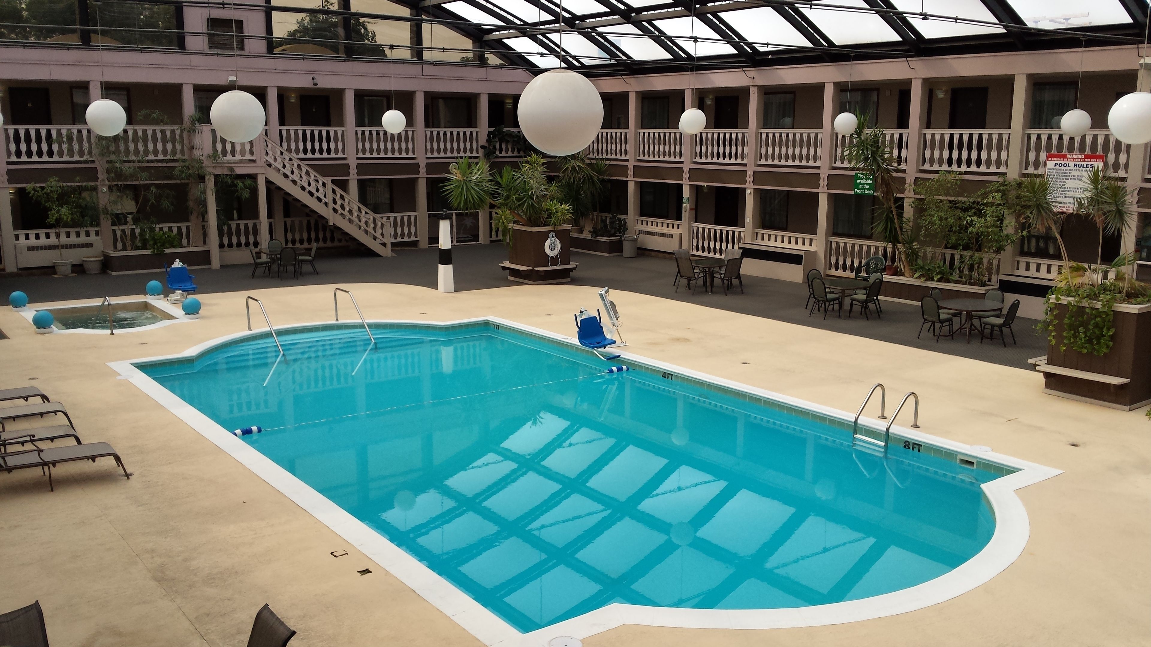 An indoor swimming pool with multiple levels of balconies, lounge chairs, and tables.