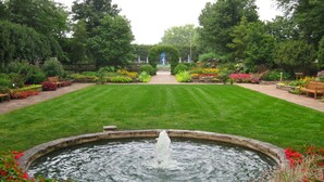 A well-maintained garden with a central fountain, surrounded by neatly trimmed grass and vibrant flower beds.