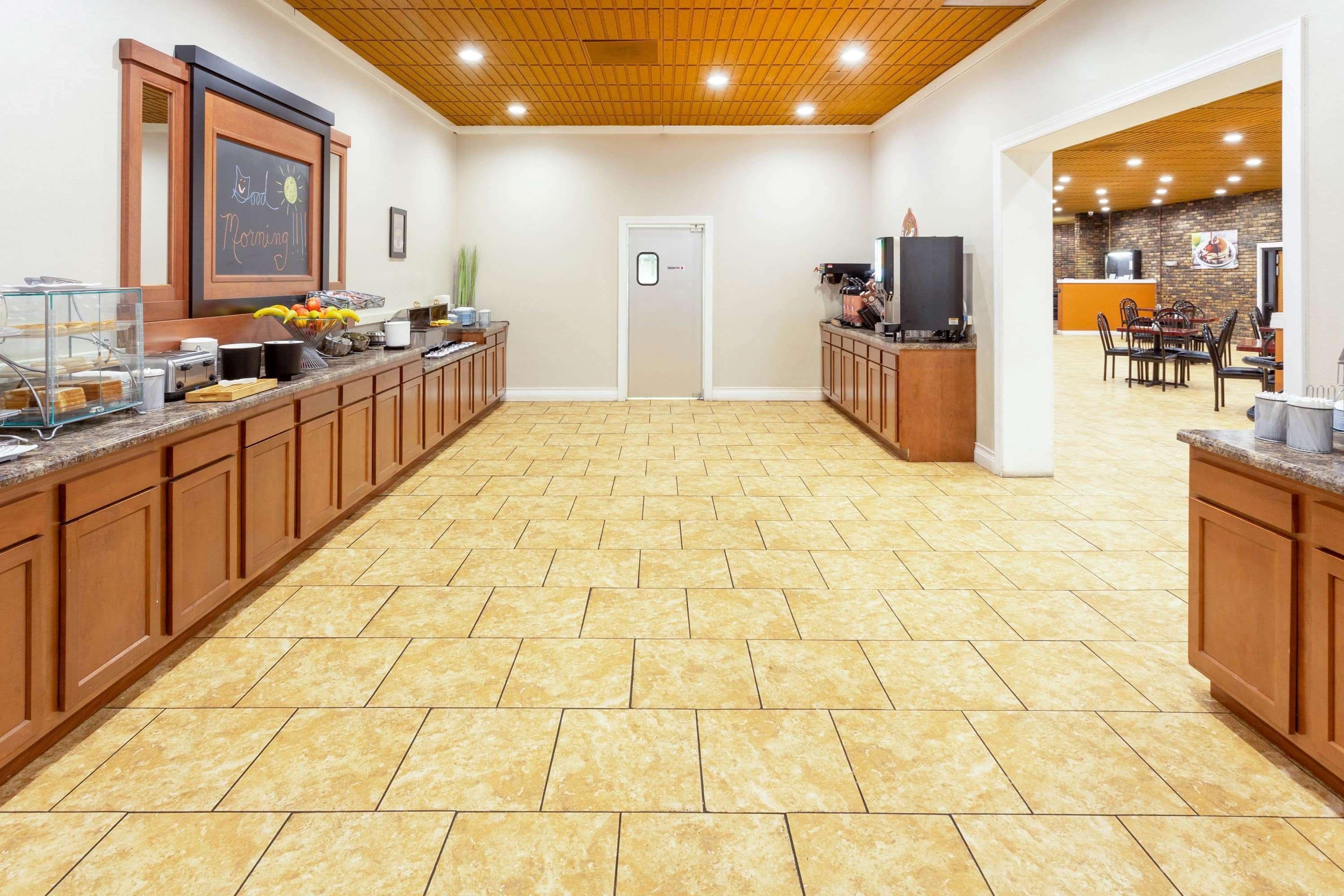 Un área de cocina amplia con armarios de madera, piso de baldosas y una pizarra con un dibujo de un gato y un sol.