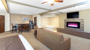 A hotel room with a bed, a sofa, a dining area with chairs, a TV, and a fireplace.