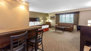 A hotel room with a kitchenette, a sofa, a chair, a desk, and a bed.