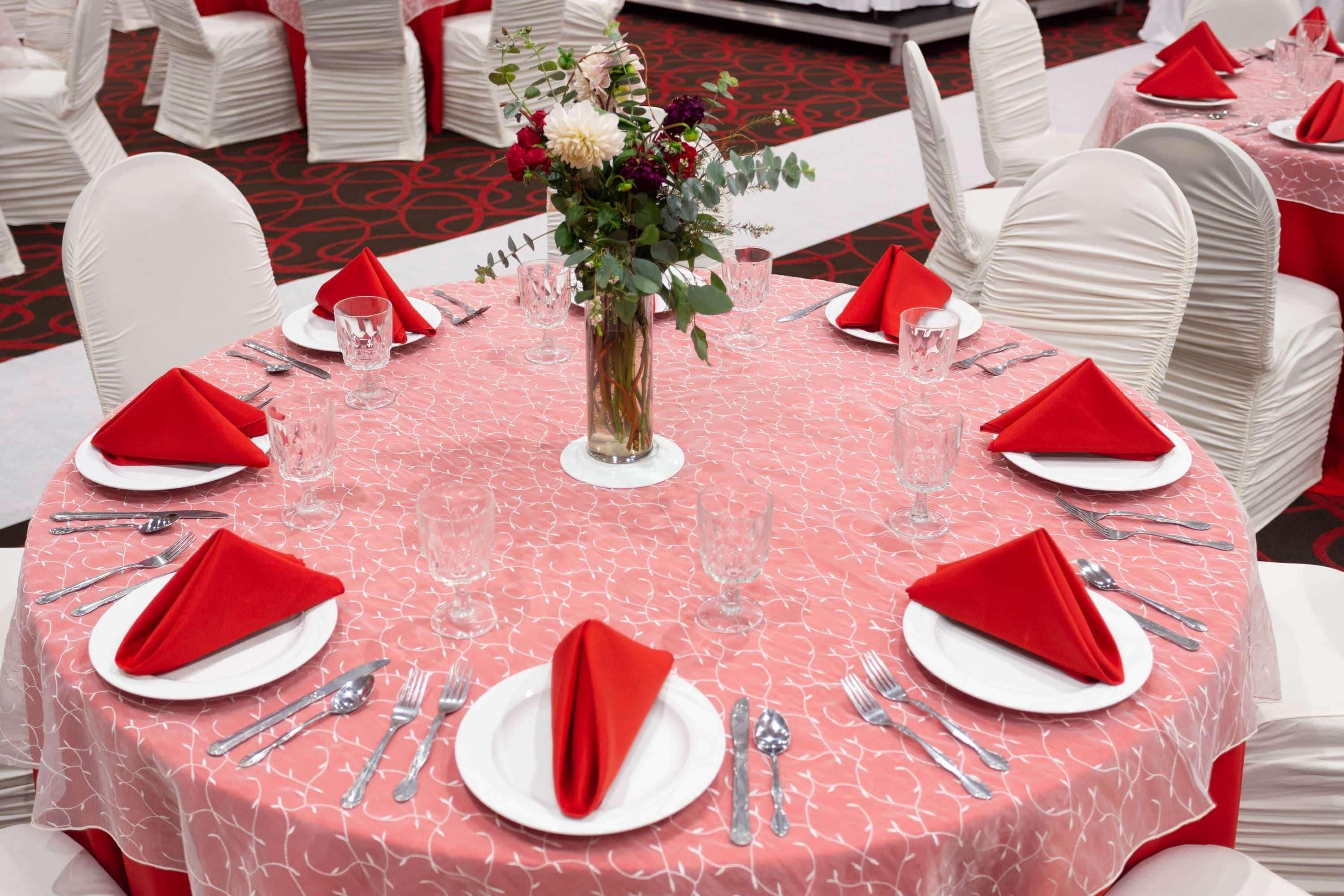 Une table ronde recouverte d’une nappe rouge, avec des chaises blanches et des serviettes rouges.