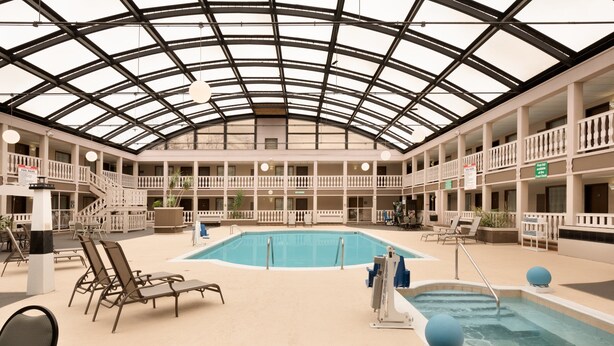 A spacious indoor pool area with a glass ceiling, multiple balconies, and lounge chairs.