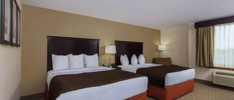 Habitación de hotel con dos camas, paredes color beige y un ventanal con cortinas.