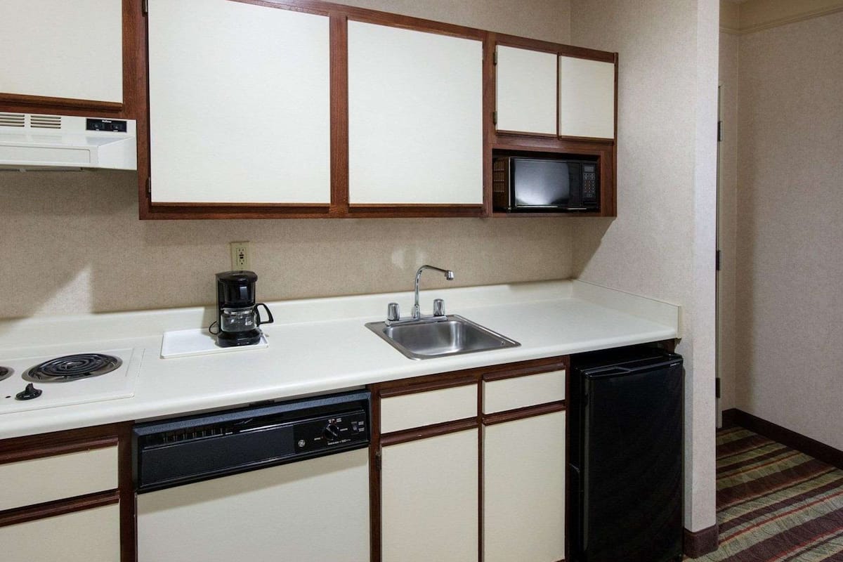 A compact kitchenette with a microwave, coffee maker, sink, and dishwasher.