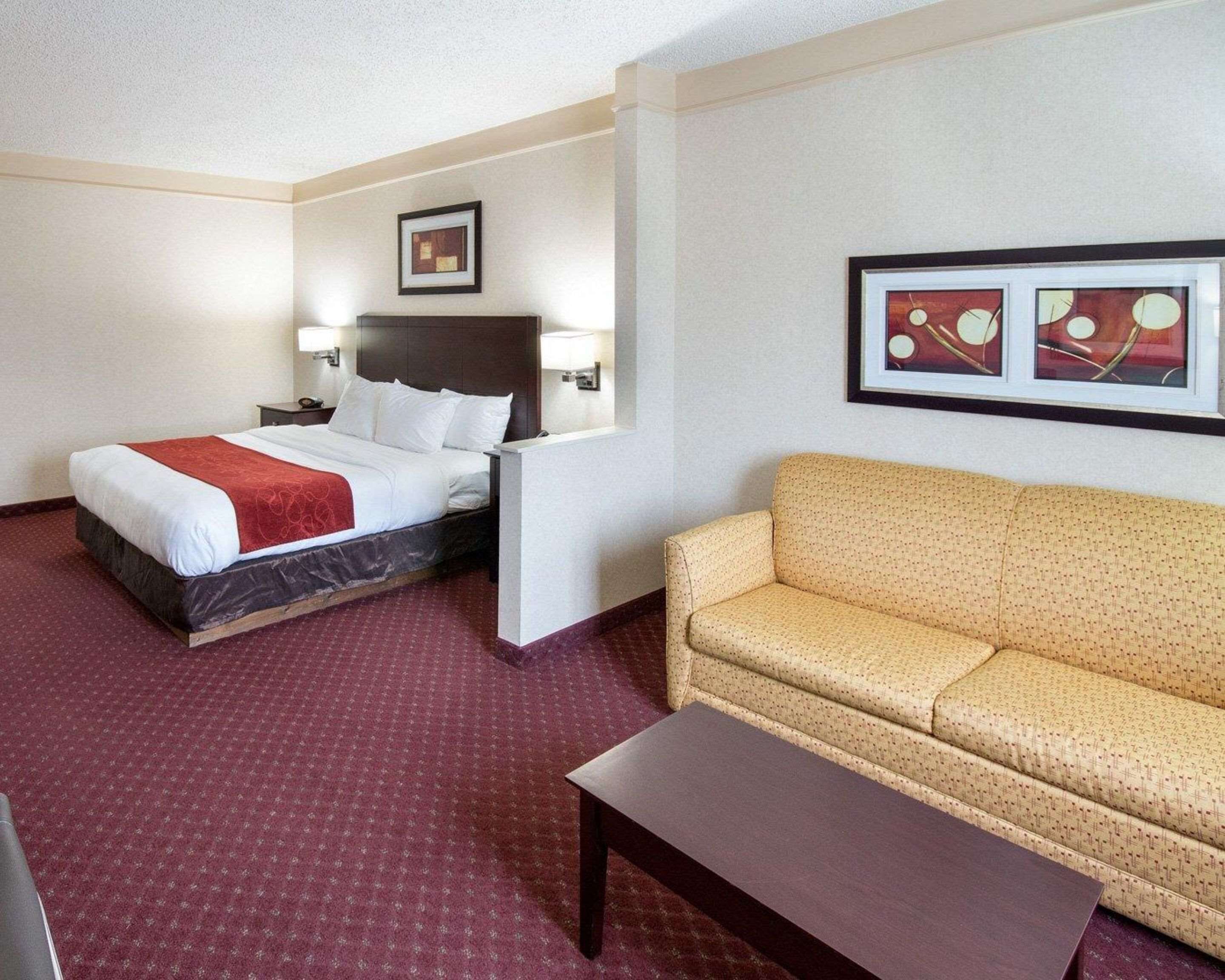Habitación de hotel con cama, sofá, mesa de centro y dos lámparas fijadas a la pared.