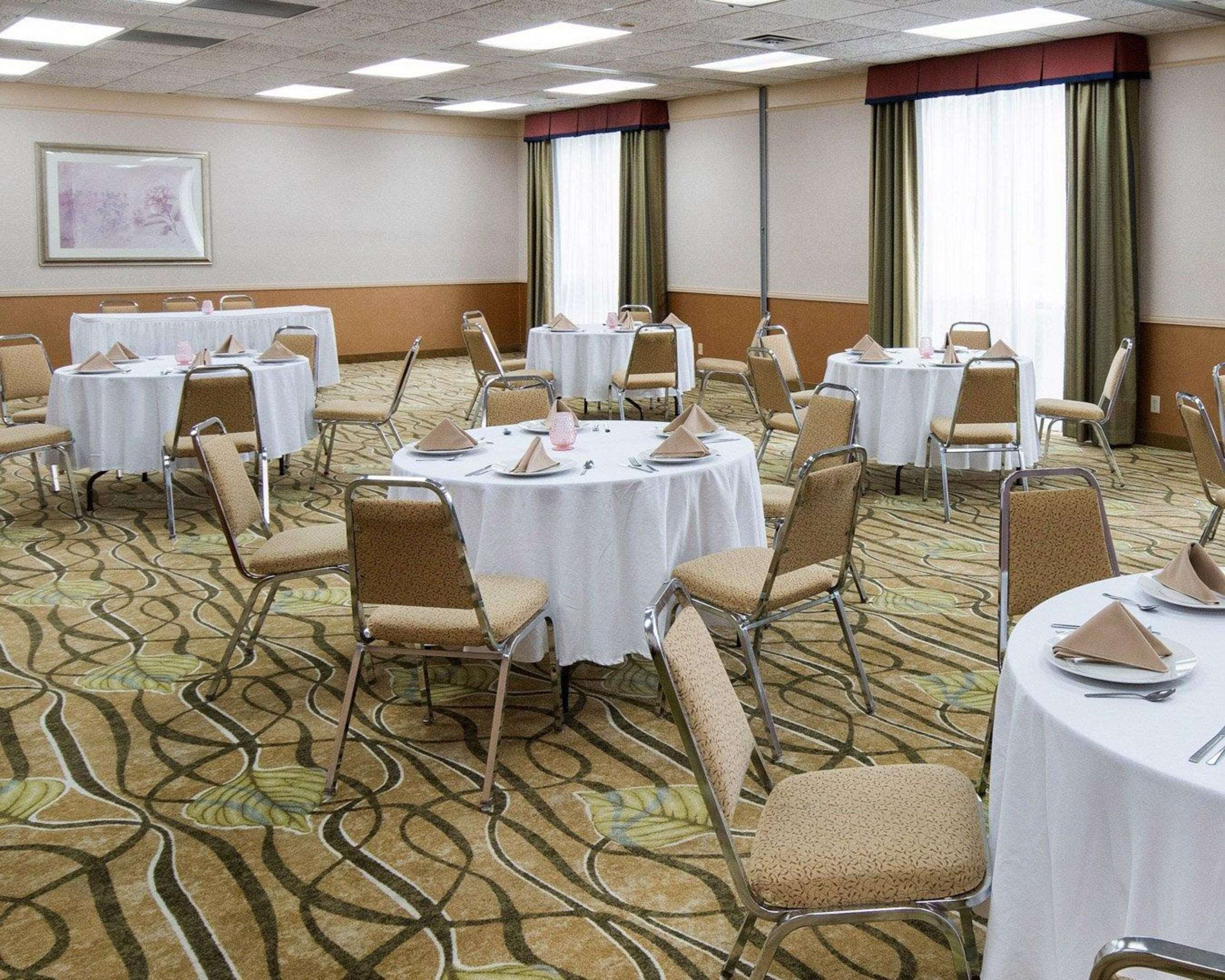 Un salón de conferencias con mesas y sillas redondas, piso alfombrado y ventanas grandes con cortinas.