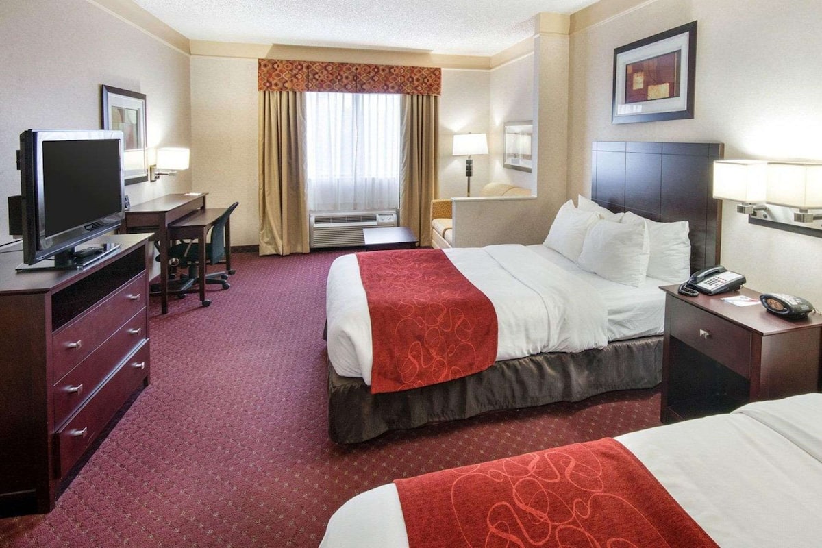 A hotel room with a bed, a desk with a TV, a chair, a lamp, and a phone on the nightstand.