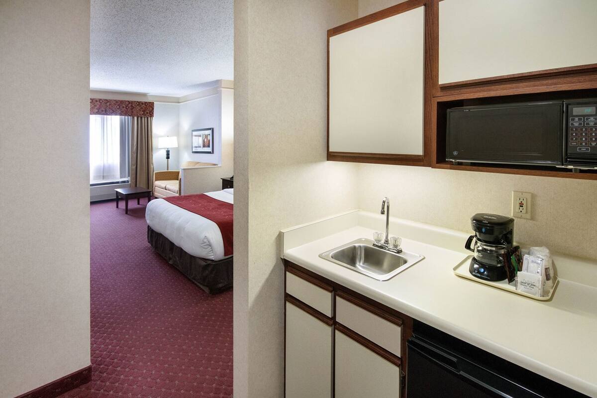 A hotel room with a kitchenette, a bed, a desk, and a window with curtains.