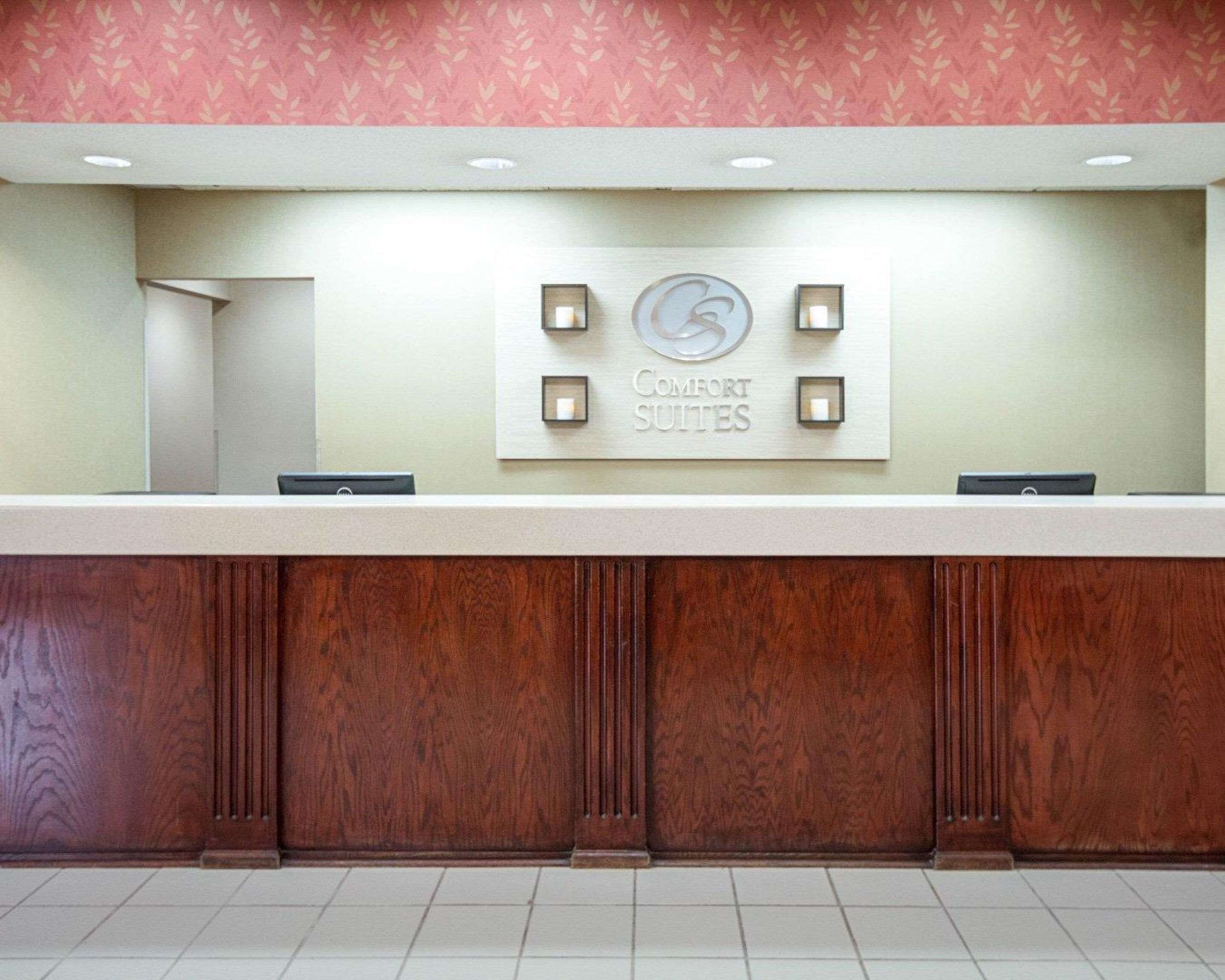 A reception desk with a sign for Comfort Suites, a wooden panel design, and a patterned wallpaper background.