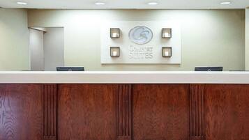 A reception desk with a sign for Comfort Suites, a wooden panel design, and a patterned wallpaper background.