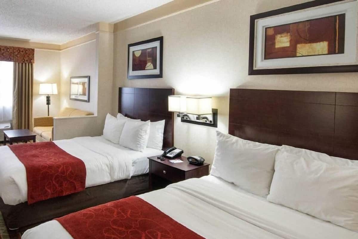 A hotel room with two beds, a nightstand with a phone, a lamp, and framed artwork on the walls.