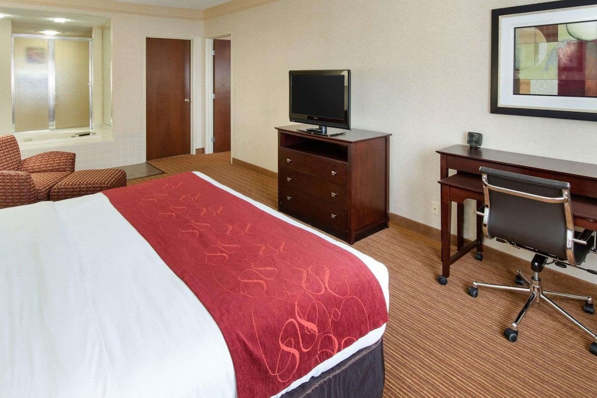 A hotel room with a bed, a desk, a chair, a television, and a bathroom with a shower and toilet.