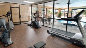 Centro de atividades físicas do hotel, com equipamentos de cardio, esteira e vista para uma piscina ao ar livre.