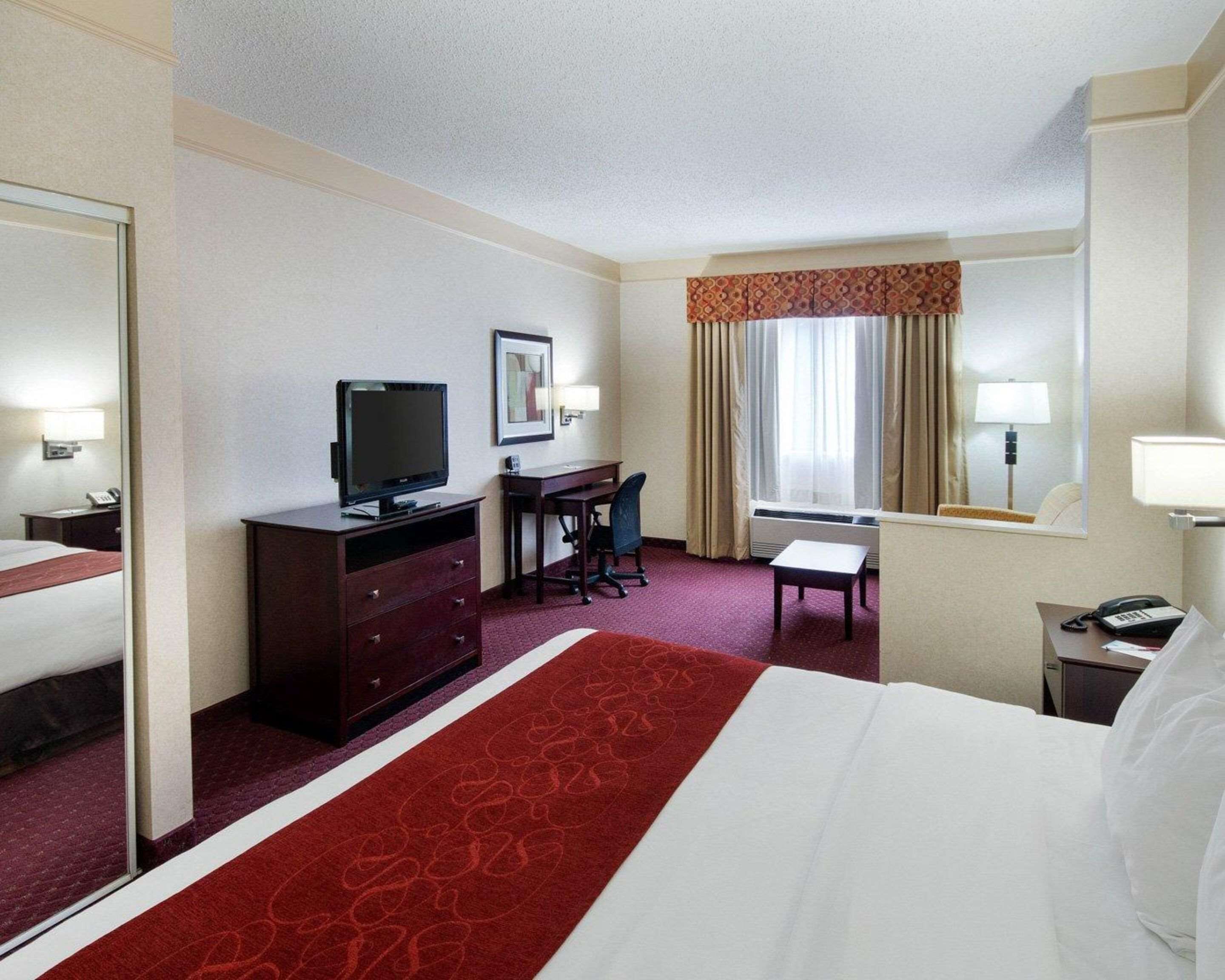 A hotel room with a large bed, a desk with a chair, a television, a small table, and a window with curtains.