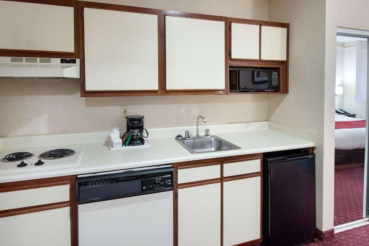 A compact hotel kitchen with a white countertop, a coffee maker, a microwave, a sink, and a dishwasher.