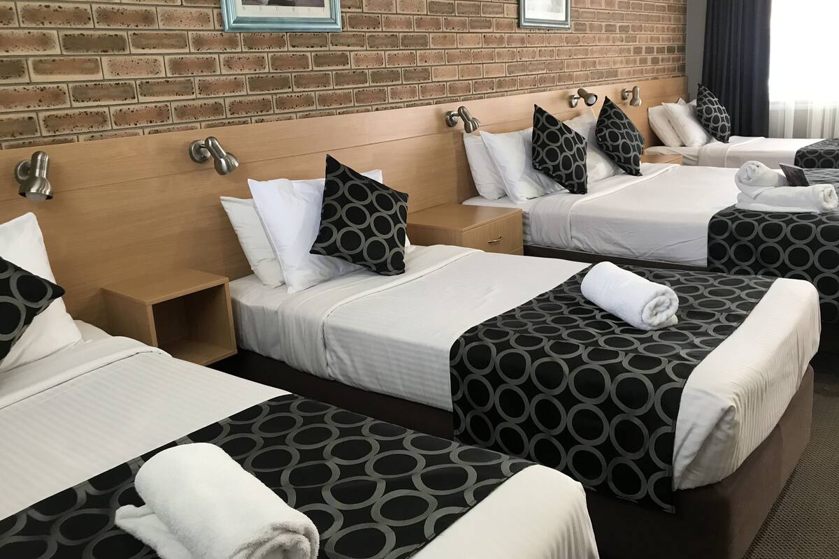 A hotel room with four beds, each with a pillow and a neatly folded towel.