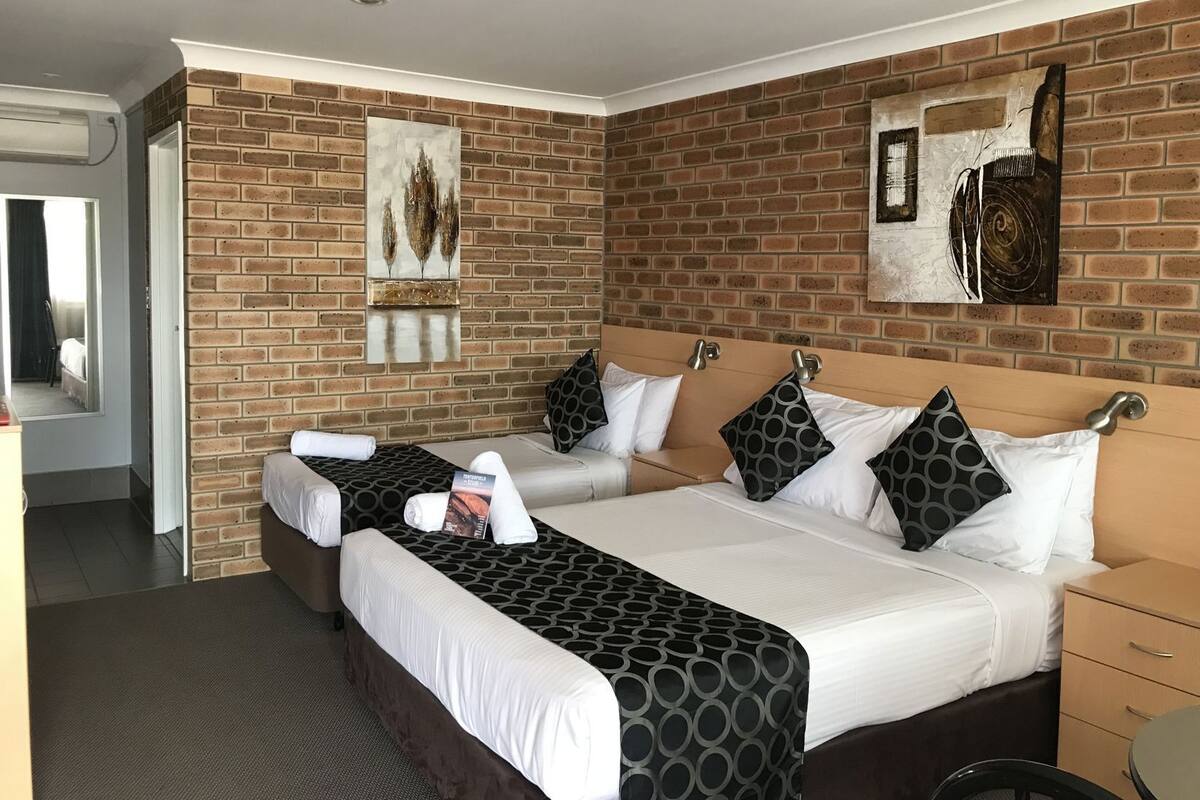 A hotel room with a brick wall, two beds, a small table, and artwork.