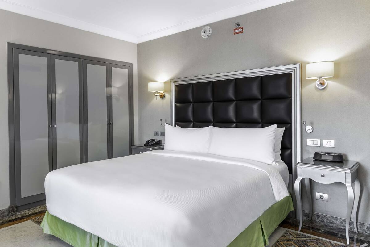 A hotel room with a large bed, a nightstand, a lamp, and a wardrobe.