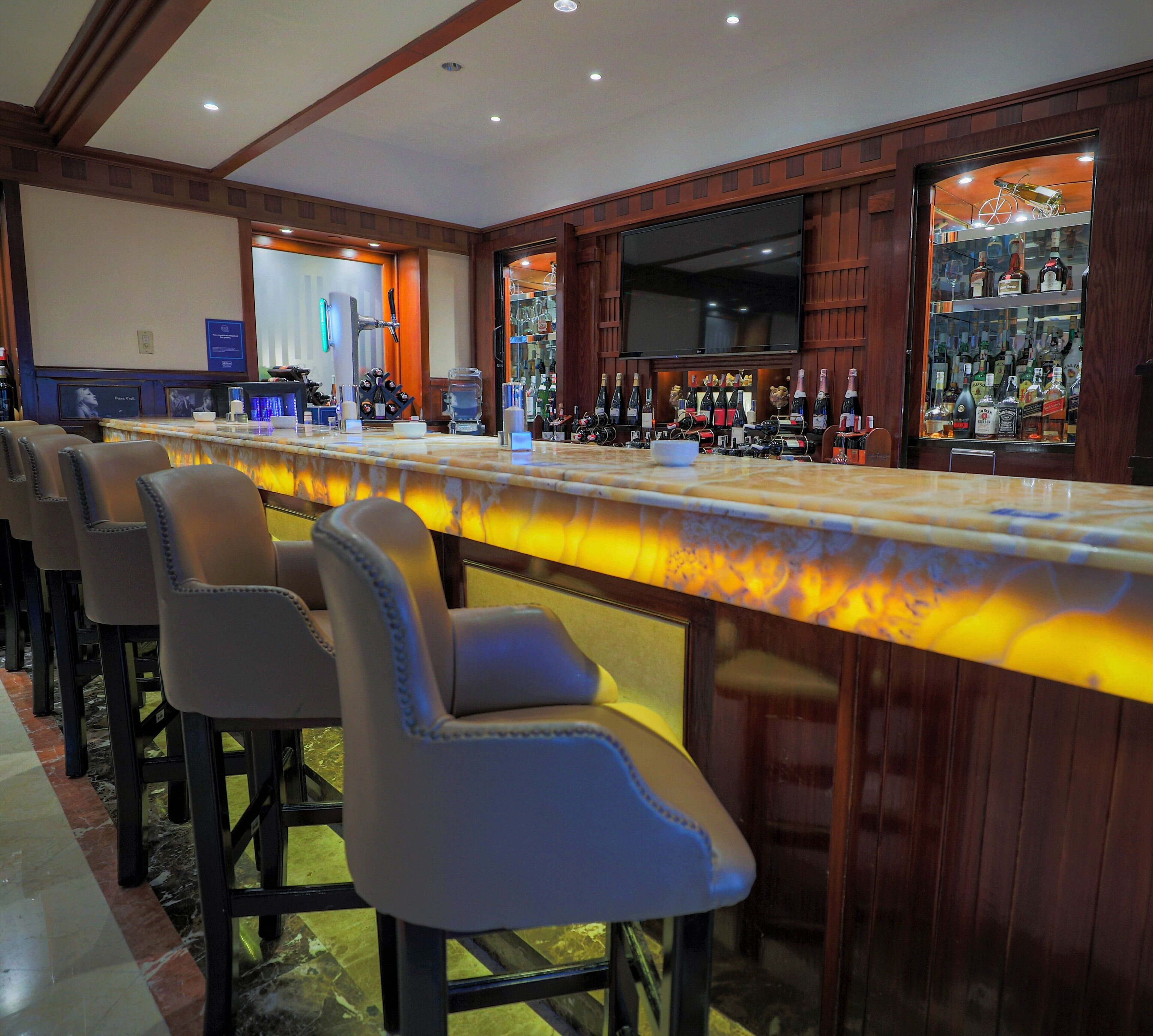 A bar area with a long counter, bar stools, and a television screen.