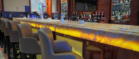 A bar area with a long counter, bar stools, and a television screen.