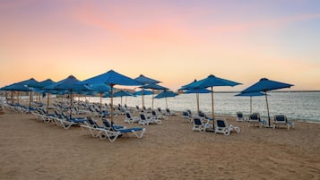 A beach with rows of sun loungers and blue umbrellas.