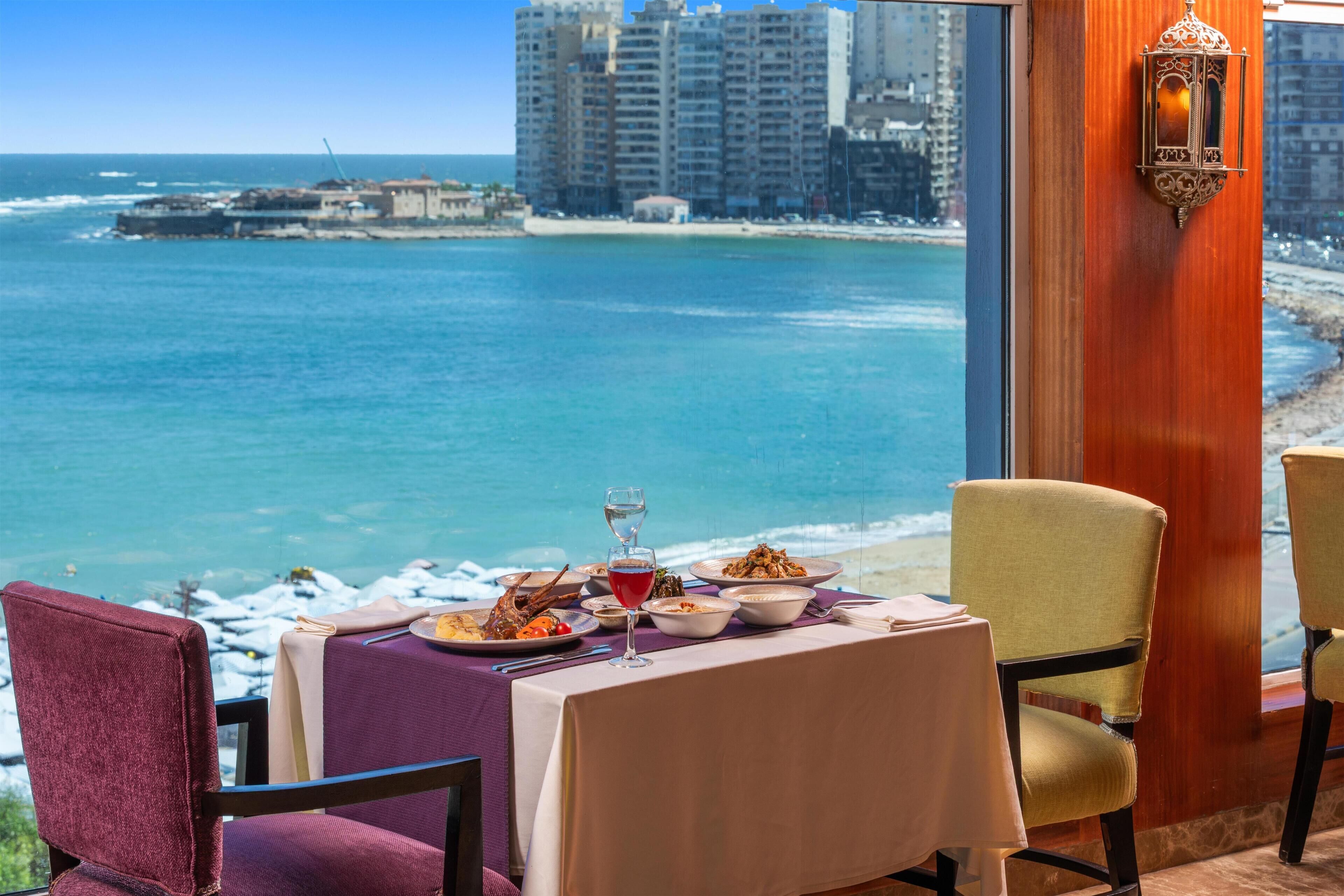 A dining table with a view of the ocean and a cityscape in the background.