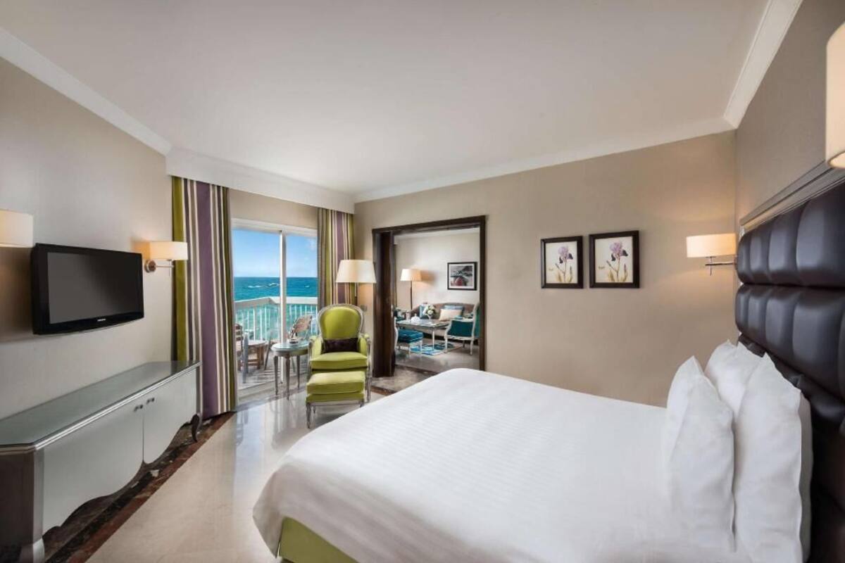 A hotel room with a bed, a television, a desk, a chair, and a view of the sea.
